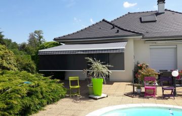 Store banne cassette aux lignes raffinées qui se distingue par son lambrequin enroulable intégré et protégé dans la barre de charge et par son éclairage à LED intégré aux bras.