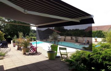 Store banne cassette aux lignes raffinées qui se distingue par son lambrequin enroulable intégré et protégé dans la barre de charge et par son éclairage à LED intégré aux bras.